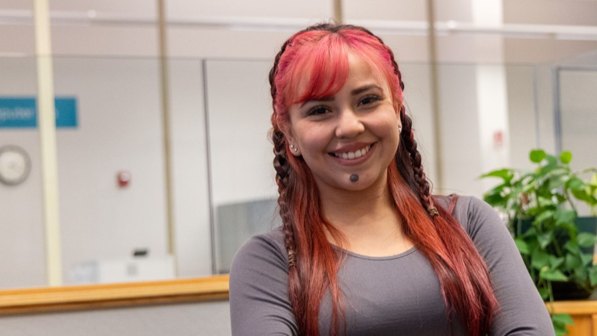 A CCC student smiles in a campus service or advising area, with an office counter and plants visible in the background.